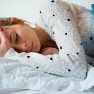 A person lying in a bed, holding their head.