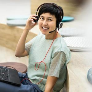 A person smiling at the camera, lifts a side of the headphones they're wearing.