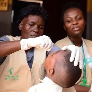 A healthcare worker giving drops to a child as another watches.
