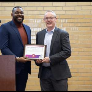 Two people holding a plaque behind a podium.