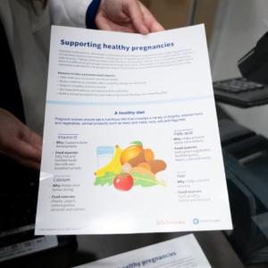 A person holding a flyer "Supporting healthy pregnancies"