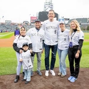 A group of people in Rockies shirts on a baseball field posing for the camera