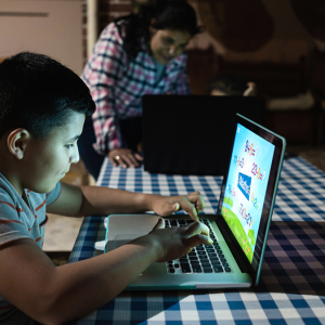 A child sitting at a desk working on a laptop, the glow from the screen lights up their face.