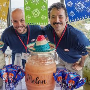 Two people smiling behind a table decorated and with three different drink dispenser
