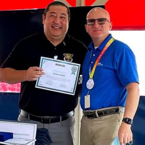 Martin in a black shirt holding a certificate next to a man in a blue shirt