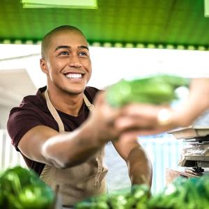 A smiling person in an apron handing something green to another.