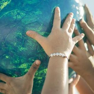 Many children's hands holding up a colorful ball.