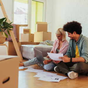 A couple sitting on the floor surrounded by moving boxes as they organize some paperwork