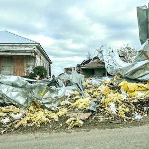 Street view of a tornado-damaged building, insulation strewn everywhere and tarps partially covering it.