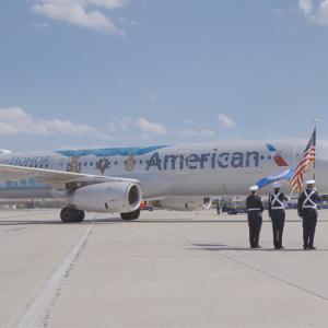 outside side view of American Air plane. Service members in uniform stand at attention on the tarmac