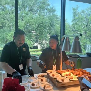 Two people serving foods under heat lamps