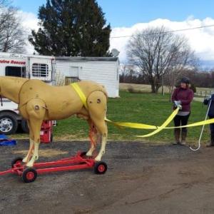 Three people with straps attached to a fake full-size horse outside.
