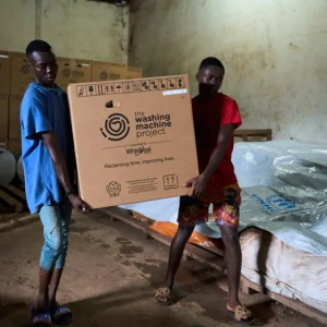 People carrying a box labeled "The Washing Machine Project"