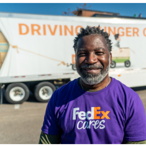 A smiling volunteer in front of a semi truck.