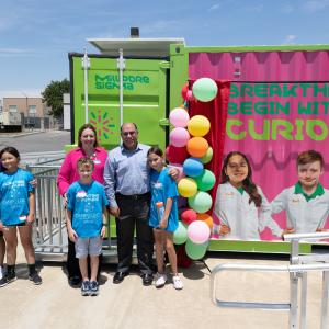 Three students and three adults stand next to their images featured on the Curiosity Cube.