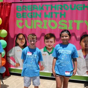 Three students next to their featured images in front of the Curiosity Cube.