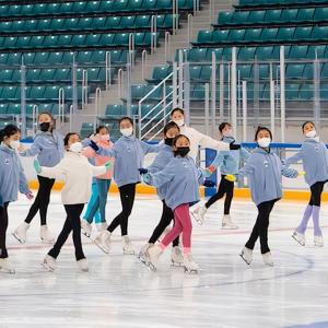 A group of children being led by an adult ice skating on a rink.