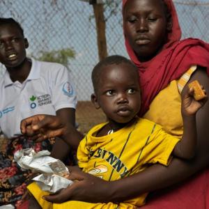 Pregnant Adheet Akeen Alhia, 20, and her child receive energy biscuits from Mary Anok Juac who works for Action Against Hunger.