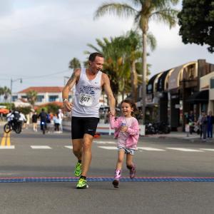 An adult participant and a child cross the finish line hand in hand during the 2026 LA Kings 5K, highlighting the event's family-friendly atmosphere and commitment to community wellness.