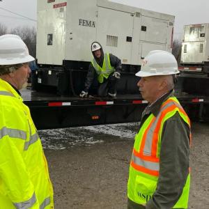 two workers outside stand beside a large trailer where two others are standing near a large generator on the trailer