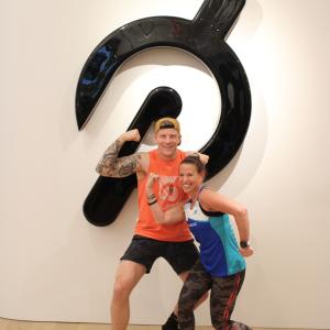 2 people flexing in front of the Peloton logo