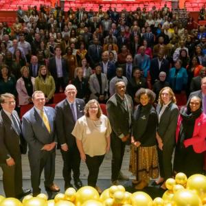 A large group of people posed on a stage and in the seating area.