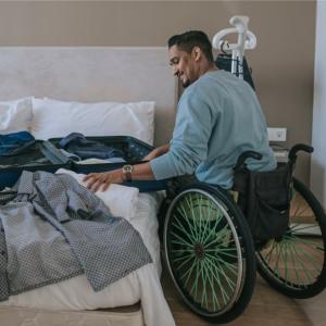 A person in a wheelchair packing clothes into a suitcase on the bed