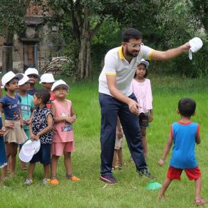 An adult shows a child a white hat, other children behind them in a group each with a matching white hat on.