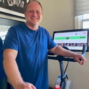 A person smiling next to an indoor bike. 