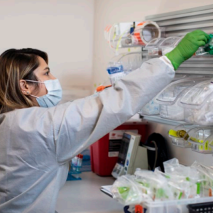 A person in protective lab gear reaching for a vial.