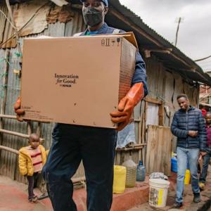 A person in protective gear holding a box in a residential area.