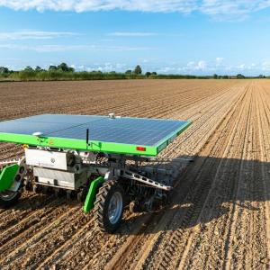 A solar panel on top of a small farm implement in a bare field. 