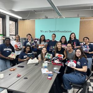 Volunteers sitting at the end of a gray table with an aqua sign saying "We are Good+Foundation"
