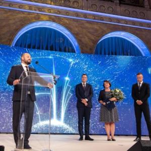 A person at a podium on a stage. Four others behind and to the side.