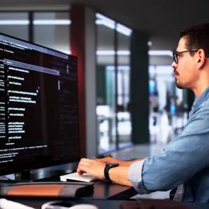 A person using a keyboard, looking at a large digital screen in a dark office setting.