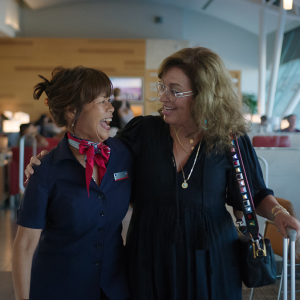Two people walking arm in arm and looking at each other, in an airport and smiling