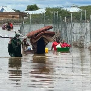 People walk through wasit-deep water, carrying belongings such as blankets