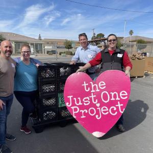 Four posed outside by a stack of milk crates. One holds a sign "the Just One project."