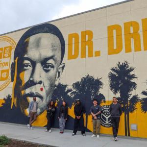 AEG team members pose outside Compton High School in front of the Andre “Dr. Dre” Young Performing Arts Center mural during a campus visit focused on career exposure and community engagement.