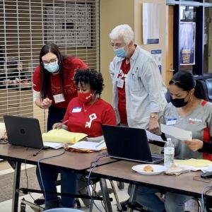 Four KeyBank volunteers seated in front of laptops ready to assist. All are wearing KeyBank red t shirts.