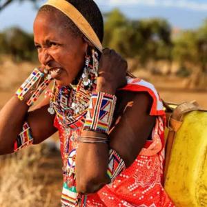 a person in Kenya, a water jug on their back with a strap around their head