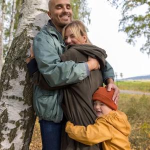 Child hugging his parents that are standing next to a tree.
