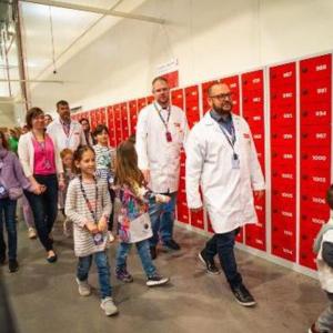 Adults and children walking down a hall lined with red boxes.