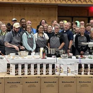 A large group of people posed behind a counter with kitchen appliances on it.