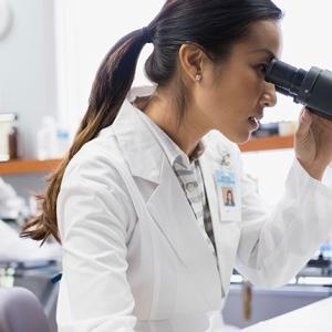 A person in white lab coat looking in a microscope