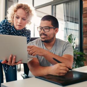 Two people looking at the same laptop in an office setting