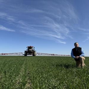 A person on one knee in a field with a machine in the background