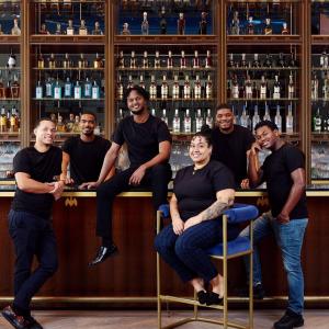 A group of students in black t-shirts posed in front of a bar