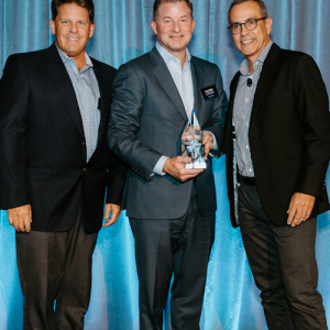 Three people stood next to each other holding an award, in front of a blue backdrop  
