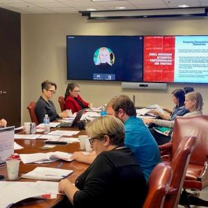 People seated around a conference table looking at a large digital presentation at the front of the room.